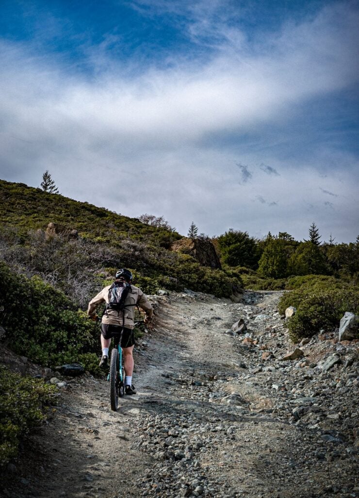 Homepage 3 Cyclist riding a gravel bike uphill on a rugged dirt road under a blue sky, illustrating the kind of gravel racing the new Colnago G5-X targets